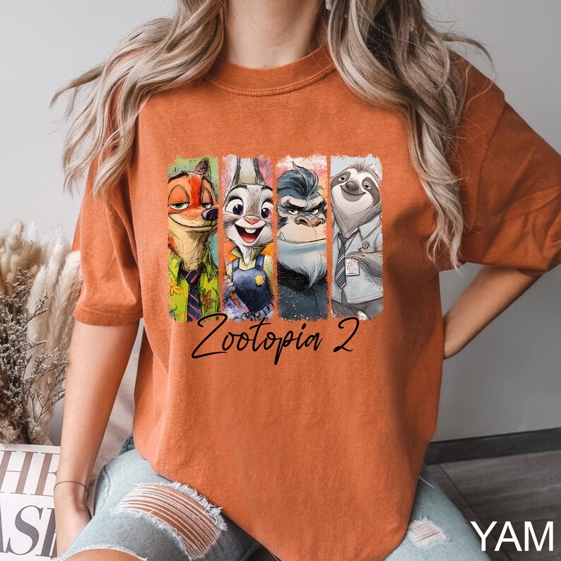 Puede incluir: Camiseta de color naranja quemado con un gr&aacute;fico colorido de personajes de la pel&iacute;cula "Zootopia 2". El dise&ntilde;o incluye a Nick Wilde, Judy Hopps, el Jefe Bogo y Flash. Las palabras "Zootopia 2" est&aacute;n escritas en cursiva debajo de los personajes.