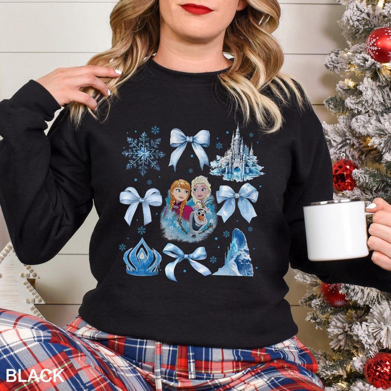 May include: Black sweatshirt featuring a design with snowflakes, bows, and a castle. The design includes images of two girls and a snowman. The word "BLACK" is printed at the bottom of the sweatshirt.