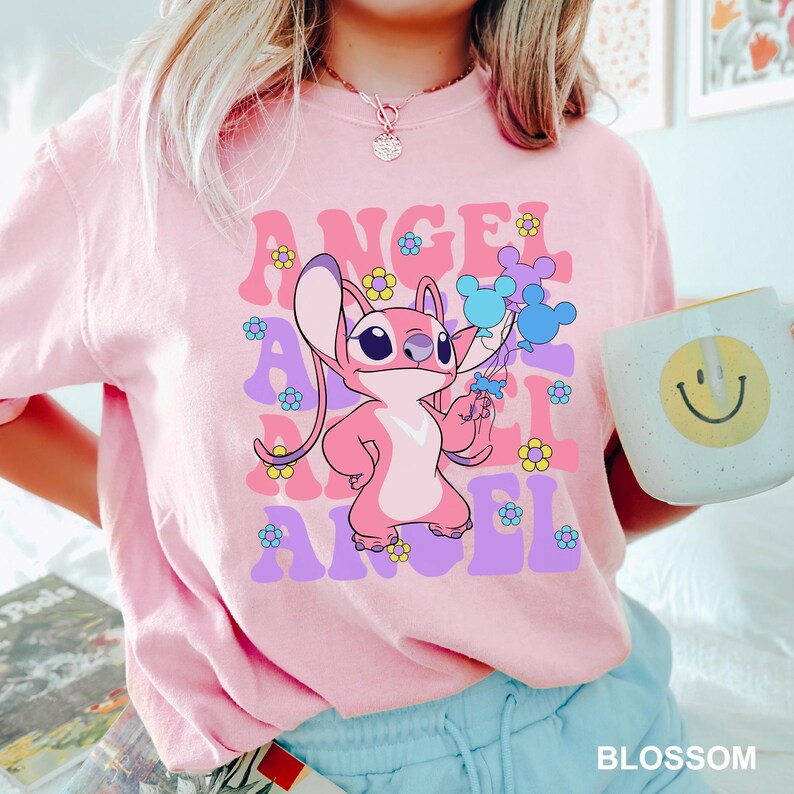May include: A light pink t-shirt featuring a cartoon character holding balloons, with the word "ANGEL" in a retro font. The shirt also has flower graphics. The word "BLOSSOM" is at the bottom.