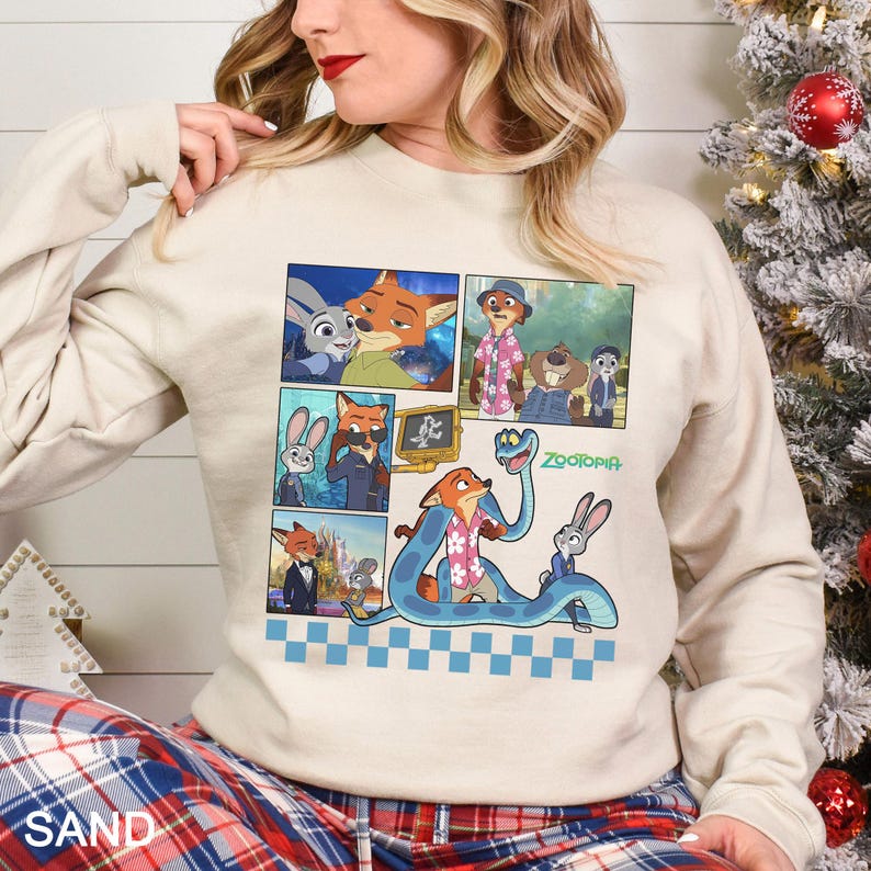 K&ouml;nnte beinhalten: Ein sandfarbenes Sweatshirt mit einem Comic-Strip-Design mit Charakteren aus dem Animationsfilm "Zootopia". Die Grafik enth&auml;lt Bilder eines Fuchses, eines Hasen und anderer Charaktere. Das Wort "Zootopia" ist in Gr&uuml;n gedruckt. Der untere Teil des Sweatshirts hat ein blau-wei&szlig;es Karomuster.