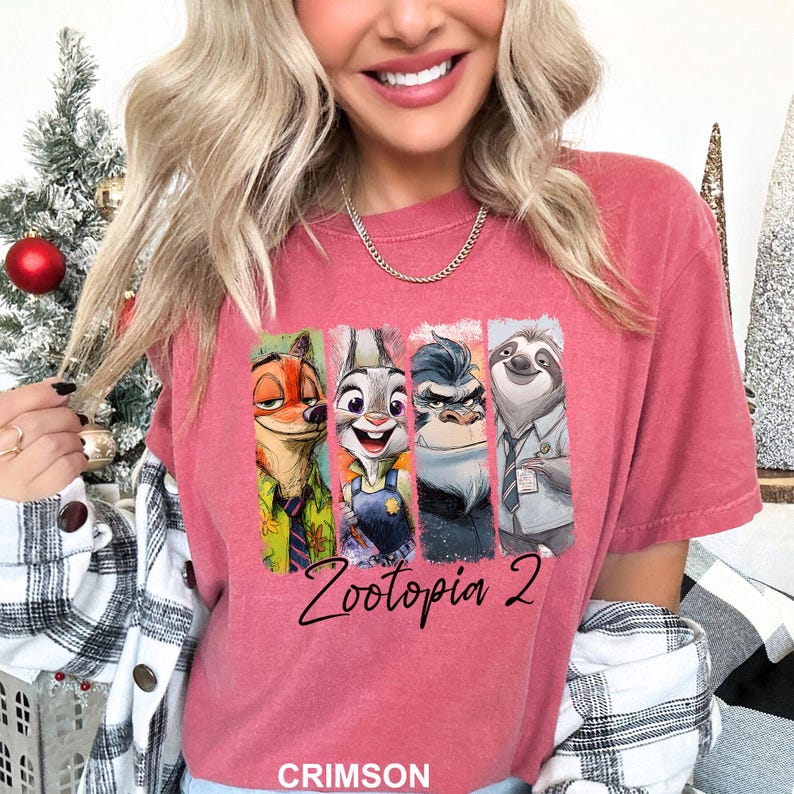 Puede incluir: Camiseta de color carmes&iacute; con los personajes de Zootopia. El dise&ntilde;o incluye a Nick Wilde, Judy Hopps, el jefe Bogo y Flash, con el texto "Zootopia 2" en letra cursiva. La palabra "CRIMSON" est&aacute; impresa en la parte inferior.