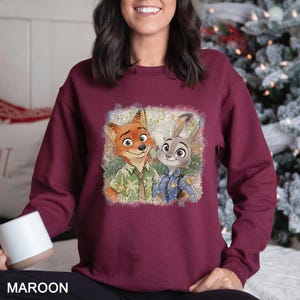 May include: Maroon sweatshirt featuring a cartoon image of a fox and a rabbit. The fox is wearing a green shirt, and the rabbit is in a blue police uniform. The word "MAROON" is printed at the bottom of the image.