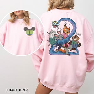 May include: Light pink sweatshirt featuring a cartoon graphic on the back with a blue snake and several animal characters. The front has a small Mickey Mouse-inspired design. The text "LIGHT PINK" is at the bottom.