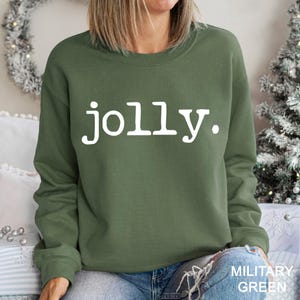 May include: Olive green sweatshirt with the word "jolly" in white block letters. The sweatshirt is a crew neck style. The words "MILITARY GREEN" are printed in white at the bottom right corner of the image.