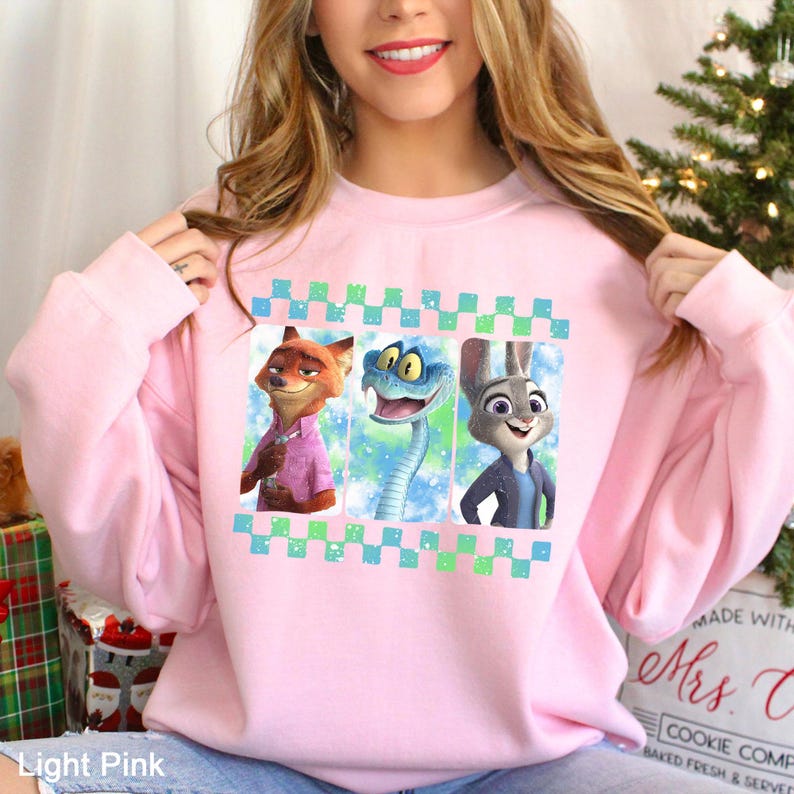 May include: Light pink sweatshirt featuring three cartoon characters in a checkered frame. The characters include a fox in a pink shirt, a blue snake, and a rabbit in a blue jacket. The text "Light Pink" is at the bottom.