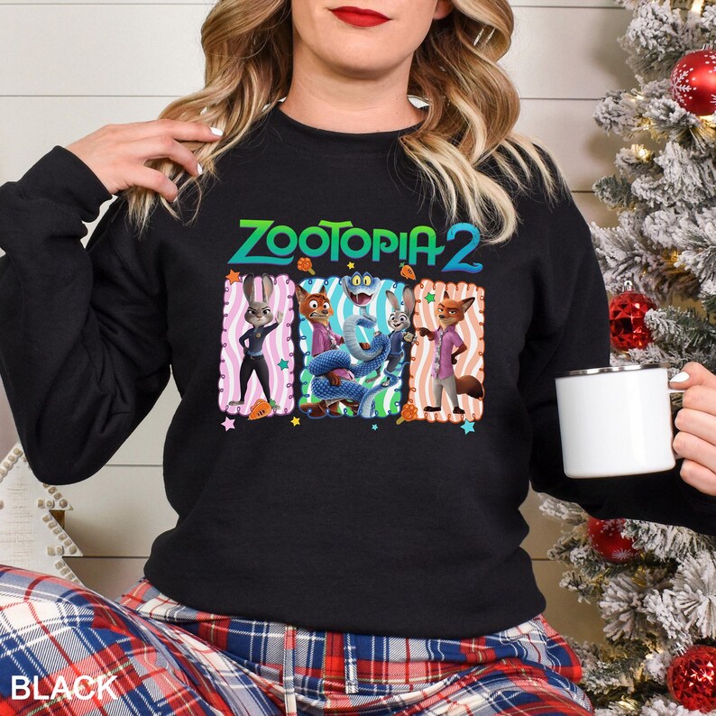 Puede incluir: Sudadera negra de cuello redondo con el texto "Zootopia 2" en verde y azul. El gr&aacute;fico incluye personajes de dibujos animados en marcos coloridos. La palabra "BLACK" est&aacute; impresa en la parte inferior.