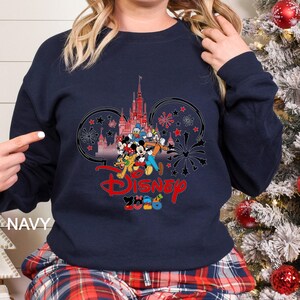 May include: Navy blue sweatshirt featuring a Disney design. The graphic includes a castle, Mickey Mouse and friends, fireworks, and the Disney logo in red. The text "2023" is below the logo. The word "NAVY" is printed on the bottom left.