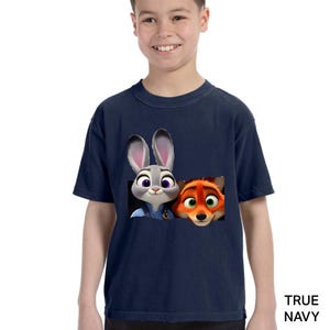 Pu&ograve; includere: T-shirt blu navy con una grafica di Judy Hopps e Nick Wilde di Zootopia. I personaggi dei cartoni animati sono in una cornice rettangolare. Il testo "TRUE NAVY" &egrave; stampato in basso a destra.