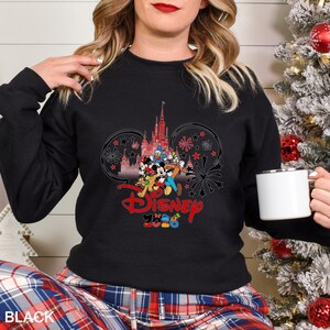 May include: Black crew neck sweatshirt featuring a Disney design with Mickey Mouse, Donald Duck, and other characters in front of a castle. The word "Disney" is in red script, with "2020" below. The word "BLACK" is at the bottom.