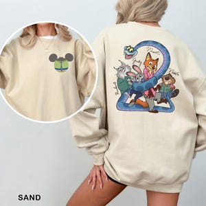 May include: Sand-colored sweatshirt featuring a cartoon graphic on the back with characters from a movie. The front has a small Mickey Mouse head design. The word "SAND" is printed at the bottom. The sweatshirt is made of a soft material.