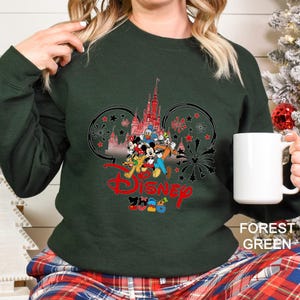 May include: Forest green sweatshirt featuring a Disney design. The design includes the Disney logo in red, a castle, and various cartoon characters. The sweatshirt is a solid color and has a crew neck.