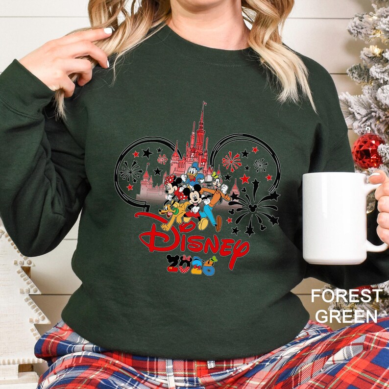 May include: Forest green sweatshirt featuring a Disney design. The design includes the Disney logo in red, a castle, and various cartoon characters. The sweatshirt is a solid color and has a crew neck.