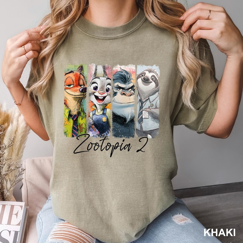 Puede incluir: Camiseta caqui con un gr&aacute;fico colorido de los personajes de Zootopia: Nick Wilde, Judy Hopps, Chief Bogo y Flash. El texto "Zootopia 2" est&aacute; impreso debajo de los personajes. La camiseta es de color neutro.