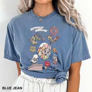 May include: Blue jean-colored t-shirt featuring a colorful graphic of characters from a popular animated movie. The design includes a donut, a carrot, and the text "You can be whatever you wish to be."
