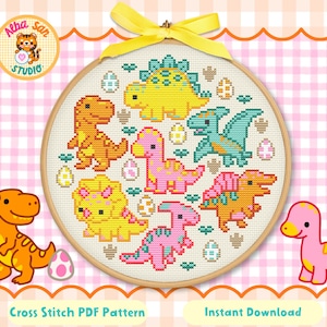 Puede incluir: Un bastidor de bordado circular de madera que contiene un patrón de punto de cruz de seis dinosaurios coloridos y varios huevos estampados. Los dinosaurios son amarillos, naranjas, rosas y verde azulado. Un lazo amarillo brillante está atado arriba.