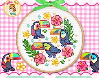Op de afbeelding: Een ronde houten borduurring met een kruissteekpatroon van drie toekans, roze hibiscusbloemen, gele sterren en groene palmbladeren. Een felgroen lint is bovenaan tot een strik gebonden. De tekst Alba San Studio is zichtbaar op de afbeelding.