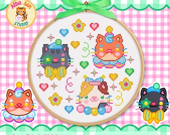 Op de afbeelding: Een kruissteekpatroon in een houten borduurring met drie gestileerde kattengezichten, kleurrijke hartjes en sterren. De katten zijn oranje, zwart en lapjeskat, versierd met strikken en hoedjes. Een groen lint is bovenaan de ring gestrikt.