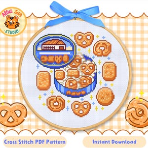 Puede incluir: Un patrón de punto de cruz que muestra una lata de galletas azul llena de pretzels y galletas, dentro de un bastidor de bordado de madera y atado con una cinta azul. El texto "Cross Stitch PDF Pattern" y "Instant Download" son visibles.