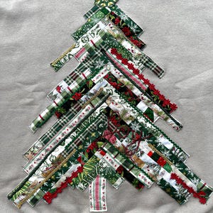 Pode incluir: Um moletom bege apresenta um design de árvore de Natal. A árvore é construída a partir de vários tecidos estampados verdes e vermelhos, incluindo xadrez e estampas florais. Acabamentos dourados e vermelhos acentuam a árvore, e uma estrela dourada a coroa.