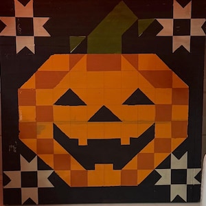 May include: A square wooden wall art piece featuring a pixelated orange pumpkin with a green stem against a black background. The design includes four white and black star-like quilt block patterns in the corners of the square panel.