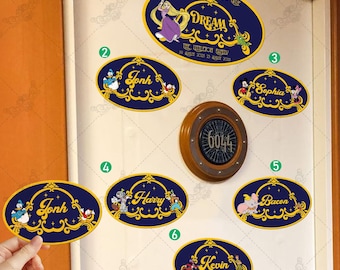 Può includere: Una porta bianca con nove adesivi ovali blu e dorati. Gli adesivi mostrano personaggi Disney e nomi come Jonh, Harry, Sophia, Bacon e Kevin. L'adesivo superiore mostra una principessa con i capelli biondi e il testo "Where dreams come true".