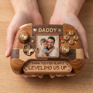 May include: A wooden game controller-shaped photo frame with the word "DADDY" and a photo of a father and child. The frame has buttons and the text "THANK YOU FOR ALWAYS LEVELING US UP".