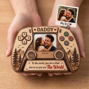 May include: A wooden game controller-shaped photo frame with the word "DADDY" and a photo of a father and child. The frame includes the text "To the world, you are a Dad, but to us you are The World." A small photo is attached that says "My Girl."