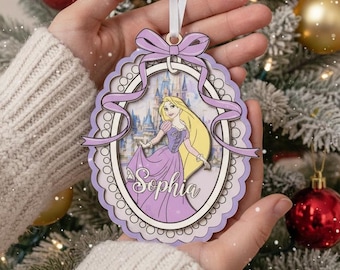 May include: A purple and white Christmas ornament featuring a princess with long blonde hair and a castle background. The ornament has a scalloped edge and a ribbon for hanging. The name "Sophia" is written on the ornament.
