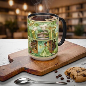 Pu&ograve; includere: Una tazza da caff&egrave; in ceramica con manico e bordo neri, piena di liquido scuro. La tazza presenta un'illustrazione verde e crema di una principessa in una biblioteca, libri e strumenti musicali. La tazza &egrave; appoggiata su un tagliere di legno.
