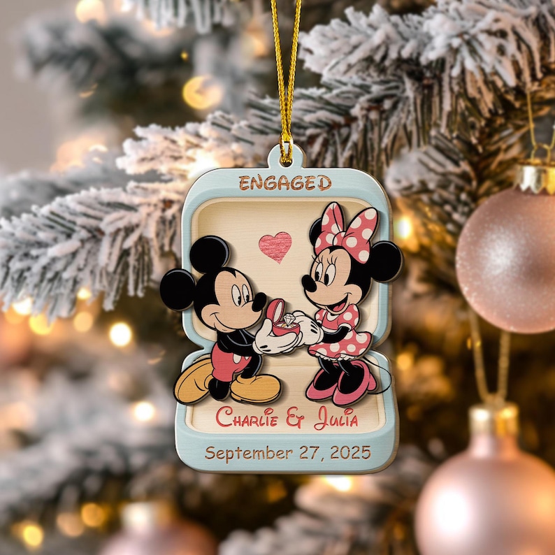 May include: A wooden Christmas ornament featuring Mickey Mouse proposing to Minnie Mouse. The ornament is shaped like a ring box, with the word "ENGAGED" at the top. The names "Charlie & Julia" and the date "September 27, 2025" are also included.