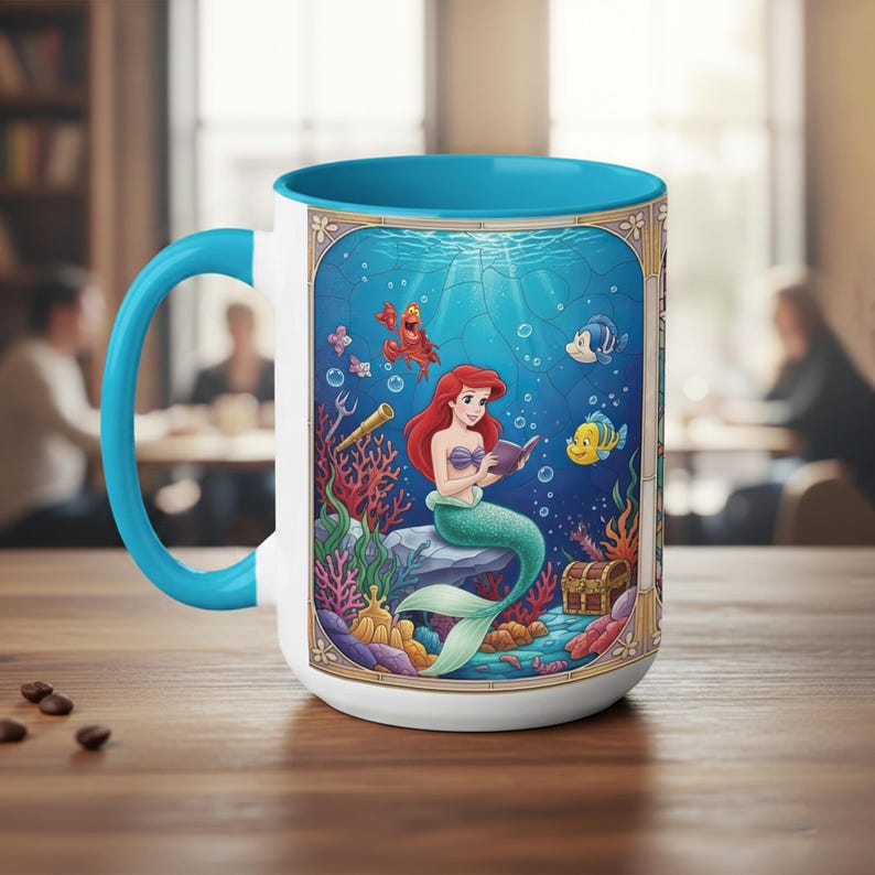Pu&ograve; includere: Tazza in ceramica bianca con interno e manico blu. La tazza presenta un'illustrazione colorata di una sirena che legge un libro sott'acqua, circondata da creature marine. Il design include un forziere e coralli.
