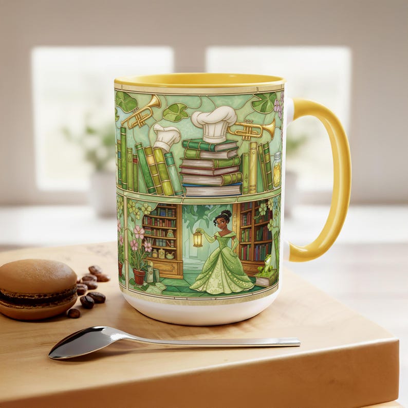 Pu&ograve; includere: Tazza in ceramica bianca con interno e manico gialli. La tazza presenta un'illustrazione dettagliata di una principessa in abito verde, circondata da libri, fiori e strumenti musicali. Un macaron e un cucchiaio sono sulla superficie di legno.