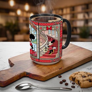 Puede incluir: Una taza de cer&aacute;mica blanca con asa negra, llena de caf&eacute; caliente. La taza presenta un colorido dise&ntilde;o de estilo vidriera de Minnie Mouse con un vestido rojo con lunares blancos. La taza est&aacute; sobre una tabla de cortar de madera con una cuchara y una galleta.