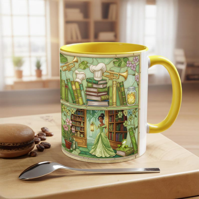 Pu&ograve; includere: Tazza in ceramica bianca con interno e manico gialli. La tazza presenta un'illustrazione colorata di una principessa in abito verde, libri ed elementi della cucina. La tazza &egrave; su una superficie di legno.