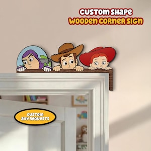 Puede incluir: Un letrero de esquina de madera con los personajes de dibujos animados Buzz Lightyear, Woody y Jessie. El letrero es marrón con el texto "CUSTOM SHAPE WOODEN CORNER SIGN" en rojo y amarillo. Un letrero ovalado amarillo en la puerta dice "CUSTOM any REQUESTS".