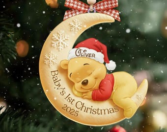 May include: A crescent moon-shaped Christmas ornament featuring a sleeping yellow bear wearing a red Santa hat with the name Oliver printed on it. The ornament includes the text Baby's 1st Christmas 2025, white snowflakes, and a red plaid bow.