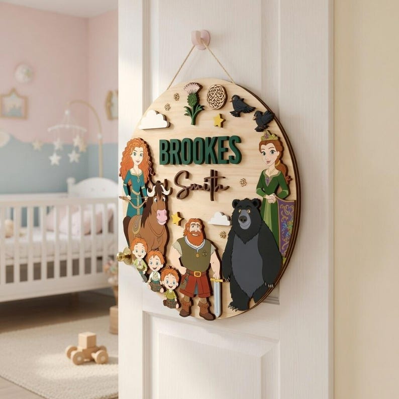 May include: A circular wooden sign with a light wood grain. It features the name "Brookes Smith" in green and white lettering, alongside cartoon characters and decorative elements. The sign is suspended from a pink hook.