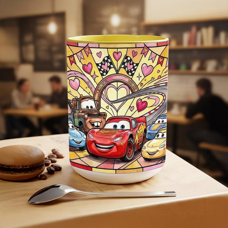 May include: A white ceramic mug with a yellow interior, featuring a colourful illustration of characters from the film Cars. The design includes race cars, hearts, checkered flags, and a race track.