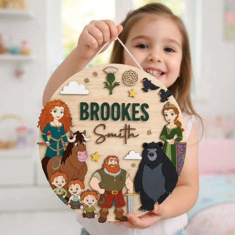 Peut inclure: Panneau rond en bois clair avec le nom "Brookes Smith" et des illustrations de personnages de dessins anim&eacute;s. Le panneau comprend un ours, un cheval et d'autres personnages, avec une ficelle blanche pour l'accrocher.