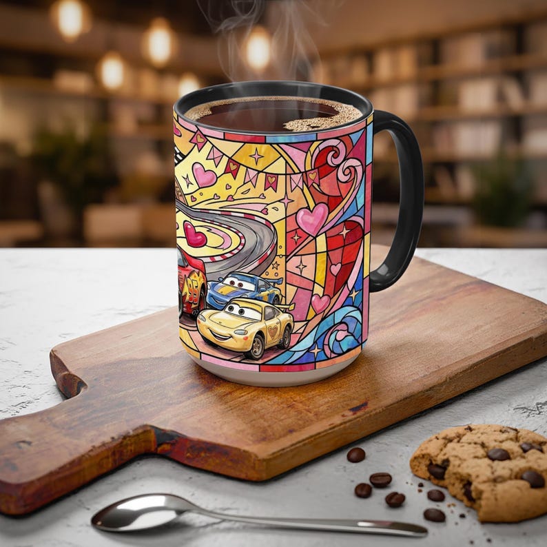 Puede incluir: Una taza de caf&eacute; de cer&aacute;mica con asa y borde negros, con un colorido dise&ntilde;o de vidriera. El dise&ntilde;o incluye im&aacute;genes de coches de carreras, corazones y una pista de carreras. La taza est&aacute; llena de caf&eacute; caliente y est&aacute; sobre una tabla de madera.