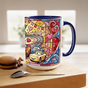 Puede incluir: Taza de cer&aacute;mica blanca con interior y asa azules, con un colorido dise&ntilde;o de vidrieras. El dise&ntilde;o incluye coches de carreras de dibujos animados, corazones y una pista de carreras. Un macaron y una cuchara est&aacute;n en primer plano.