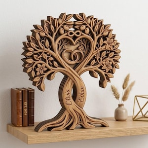 May include: A wooden tree sculpture with intertwined trunks, carved with leaves, flowers, and olives. A heart-shaped cutout in the center features wedding rings and an infinity symbol. The names "Olivia" and "Ethan" are engraved on the trunks.