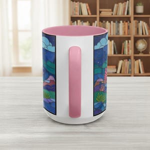 Puede incluir: Taza de cer&aacute;mica blanca con interior y asa rosa. La taza presenta un dise&ntilde;o de paisaje colorido con tonos azules, verdes y morados, que representa una escena nocturna con estrellas y nubes. El asa es de color rosa liso.