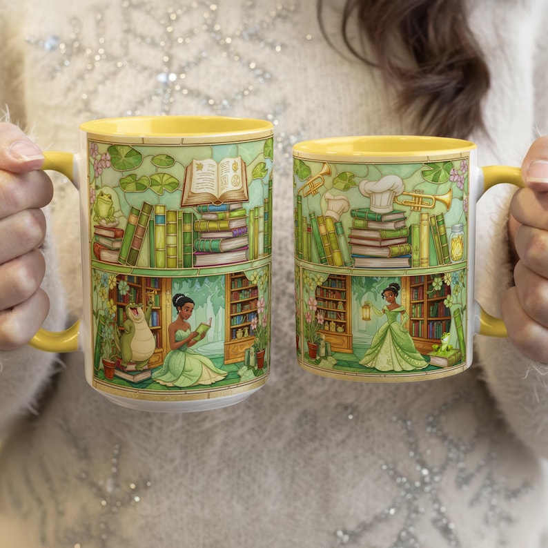 Pu&ograve; includere: Due tazze in ceramica con manici e bordi gialli. Ogni tazza presenta un'illustrazione dettagliata di una scena di biblioteca con libri, una rana e una principessa in un vestito verde. Le tazze sono tenute da una persona.