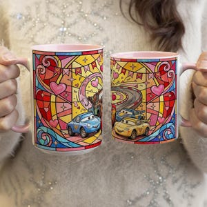 Puede incluir: Dos tazas de cer&aacute;mica con interiores y asas rosas. Cada taza presenta un colorido dise&ntilde;o de vidrieras con corazones, estrellas y coches de dibujos animados. Una taza tiene un coche azul y la otra tiene dos coches amarillos. Las tazas son sostenidas por una persona.