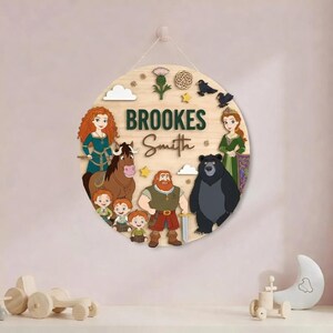 Peut inclure: Panneau rond en bois avec le nom "BROOKES Smith" en vert et divers personnages de dessins anim&eacute;s. Le panneau pr&eacute;sente un cheval, un ours et plusieurs personnes, avec des &eacute;l&eacute;ments d&eacute;coratifs comme des nuages et des &eacute;toiles.
