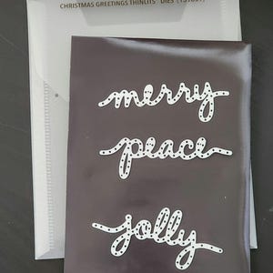 May include: A set of three white metal dies with a dotted pattern. The dies spell out the words "merry", "peace", and "jolly".