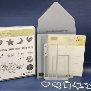 Può includere: Una collezione di materiali per il crafting, tra cui un set di timbri con la scritta "Wood Words" con vari timbri e frasi come "Hello Friend" e "Fresh Treats". Sono inclusi anche fustelle metalliche e una fustellatrice Big Shot.