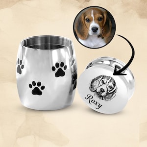 May include: Silver pet urn with paw prints and a separate lid with a black and white photo of a dog and the name "Roxy" engraved on it.