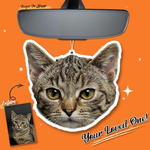 May include: A car hanging ornament featuring a detailed image of a tabby cat's face. The ornament is suspended from a rearview mirror against an orange background. Text reads "Your Loved One!"